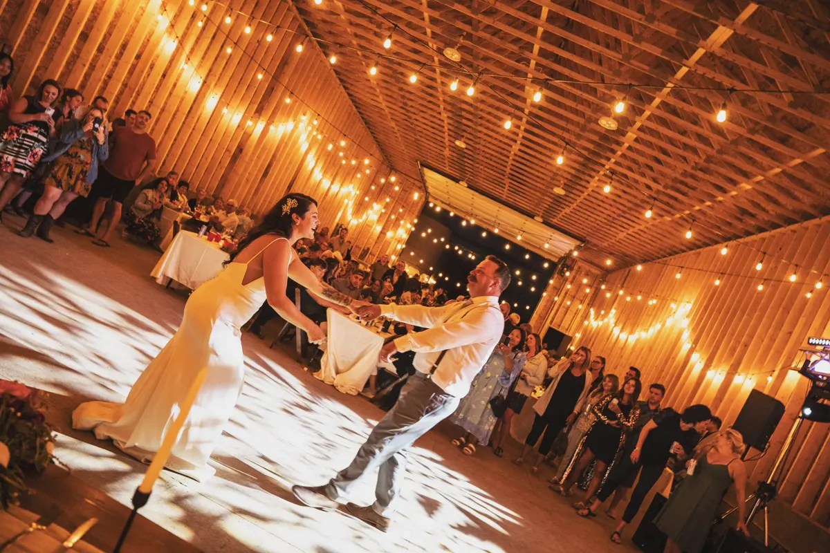 Bride and groom swinging out on the first dance in a barn strung with lights