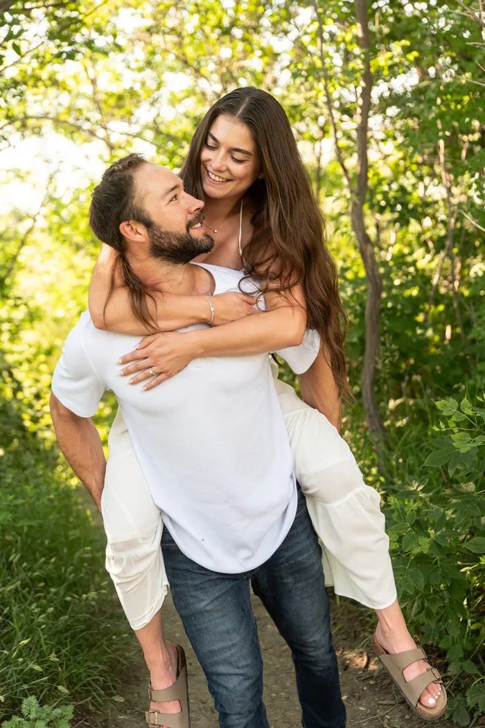Woman on her fiancé’s back, laughing on a leafy trail