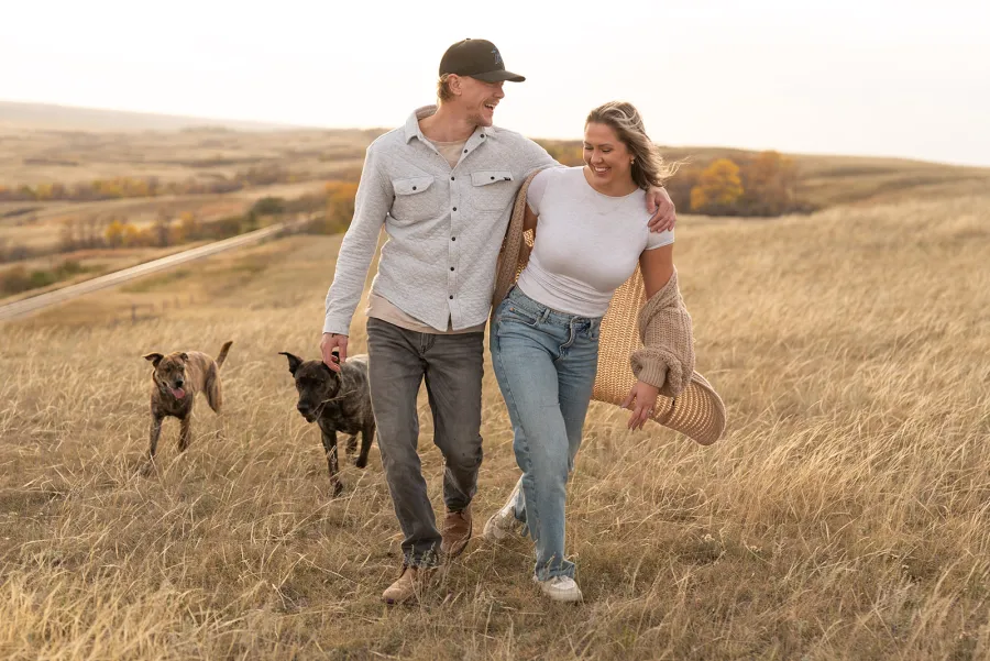 Couple walking through prairie grass with their two dogs