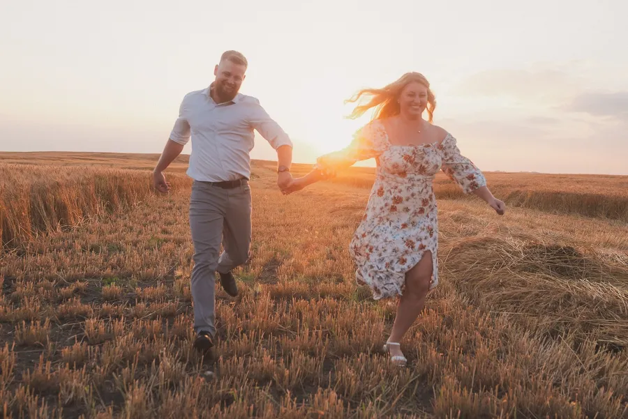 Couple running hand in hand across a stubble field at sunset