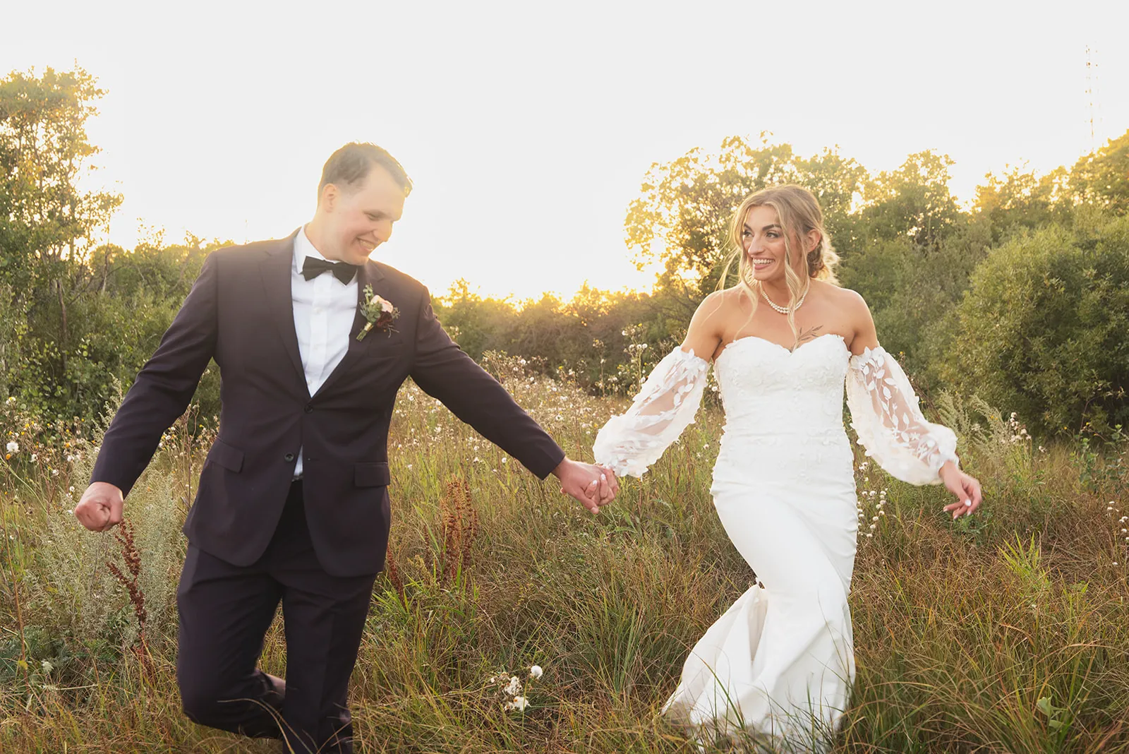 A bride and groom running hand in hand through tall prairie grass at golden hour