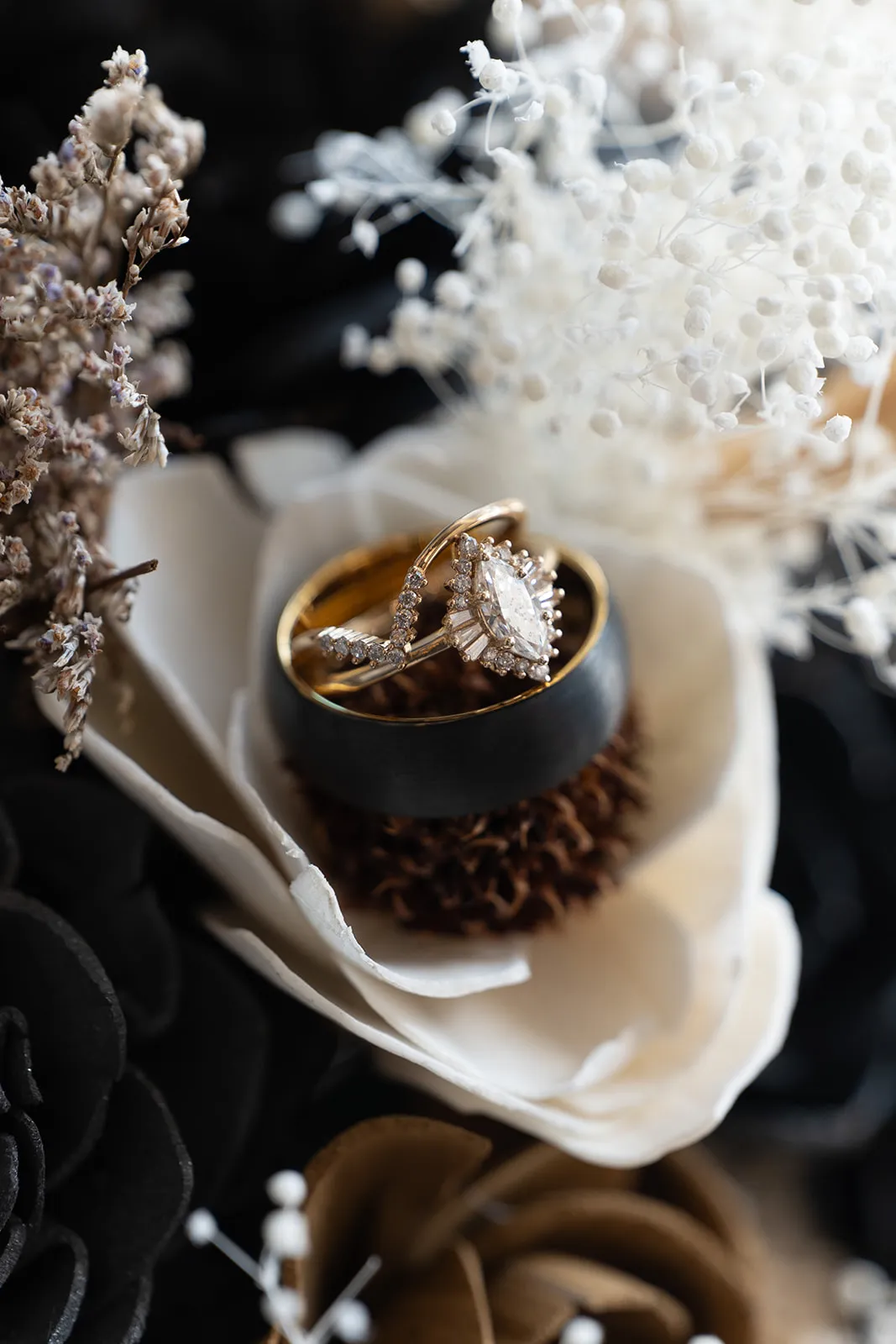Wedding rings resting in a cream wooden flower among dried baby’s breath