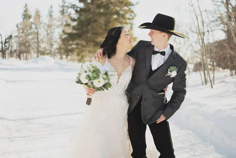 Bride and cowboy groom laughing in the snow
